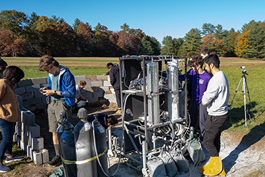 students standing outside in a field with a large engine