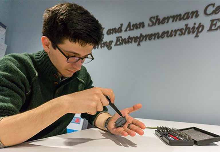 student with glasses looking down while holding component of a watch screwing a piece in his palm