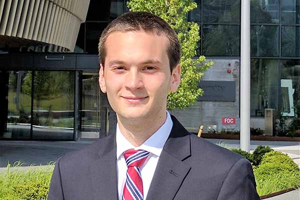 male student in business suite with business building in background