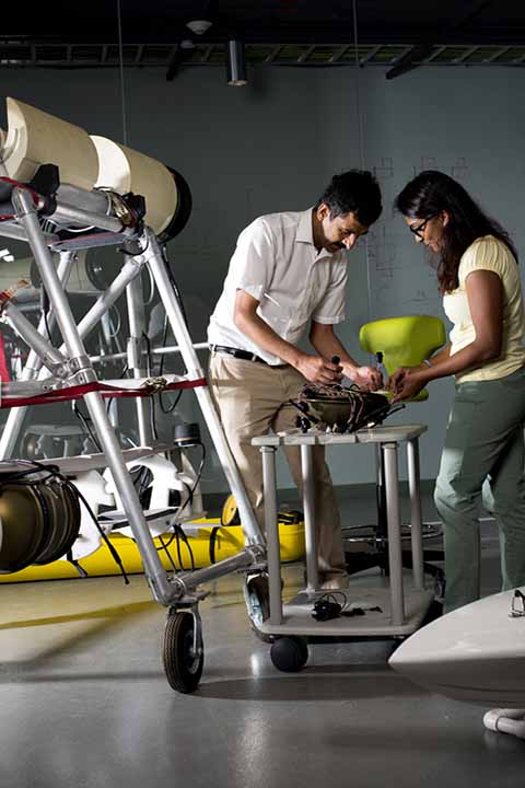 student and professor working with wires on robots on table